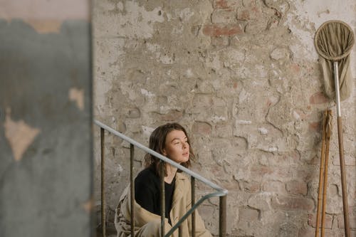 倾斜在棕色混凝土墙上的棕色外套的女人 · 免费素材图片