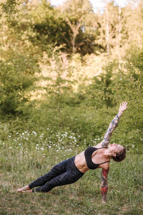 在草地上表演侧板姿势的纹身的女人 · 免费素材图片