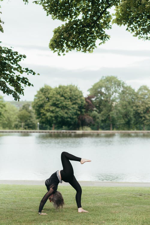 无法识别的女人在河岸边表演一个腿轮姿势 · 免费素材图片