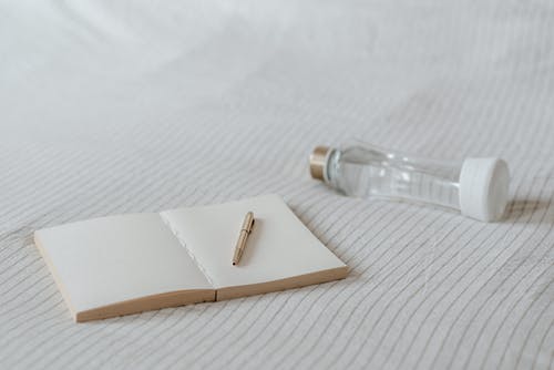 在床上的装饰瓶附近的空记事本 · 免费素材图片