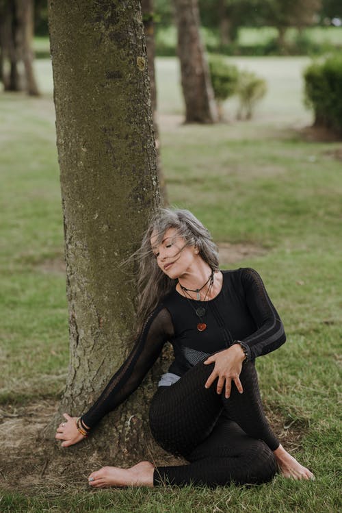 正念的女人表演坐在树旁的扭曲姿势 · 免费素材图片
