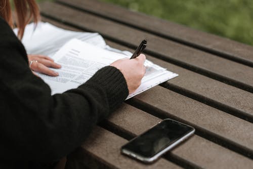 女人在手机附近的文本中记笔记 · 免费素材图片