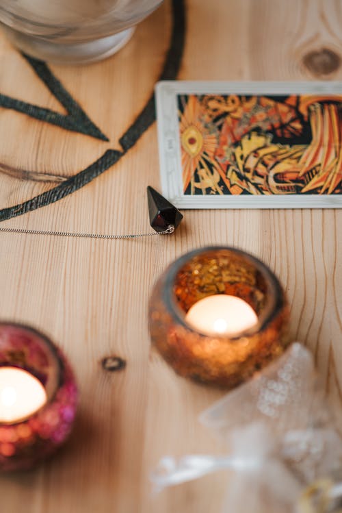 木制的桌子上塔罗牌附近燃烧的蜡烛 · 免费素材图片