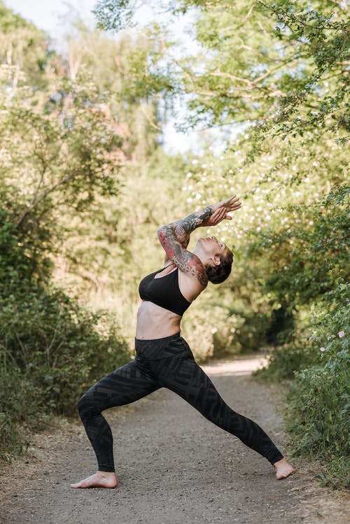 在树之间的通路上练习瑜伽的纹身的女人 · 免费素材图片
