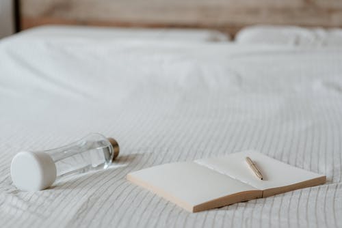 有笔的空白的笔记本在床上的小瓶附近 · 免费素材图片