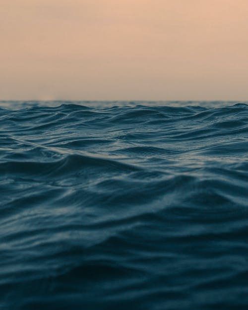 波浪海洋与地平线在日落时的天空下 · 免费素材图片