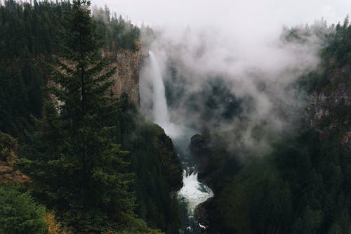 在山区地形与常绿森林对多云的天空中的瀑布 · 免费素材图片