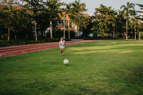 在绿草地上踢足球的白衬衫的男孩 · 免费素材图片