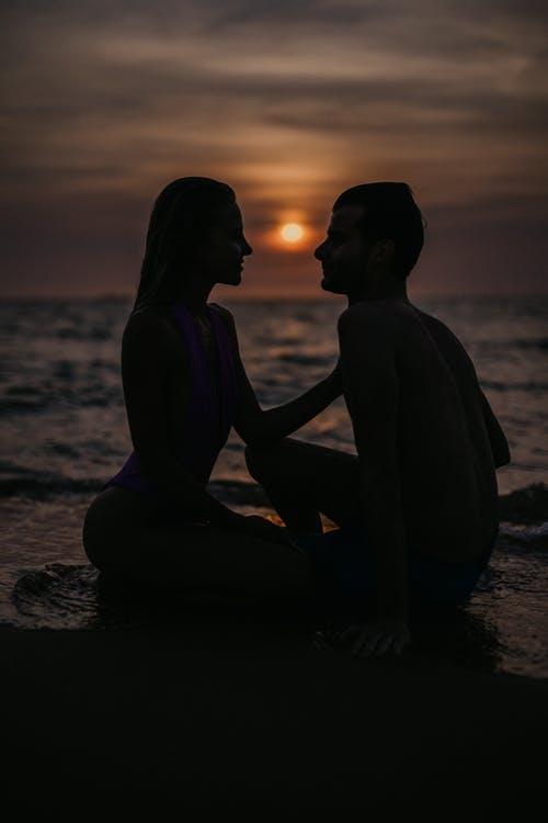 2名妇女在日落时坐在海滩上的剪影 · 免费素材图片