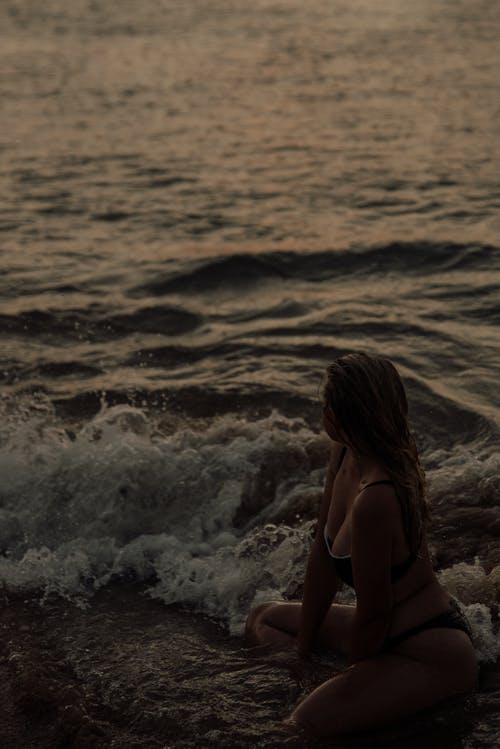 黑色比基尼坐在日落海滩上的女人 · 免费素材图片