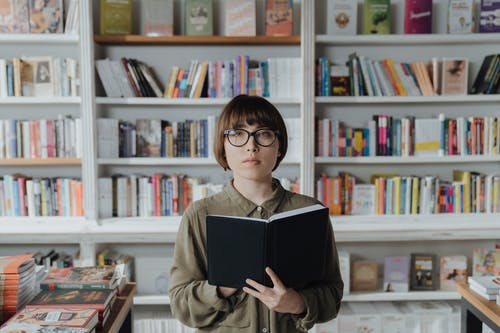 拿着黑书的棕色外套的女人 · 免费素材图片