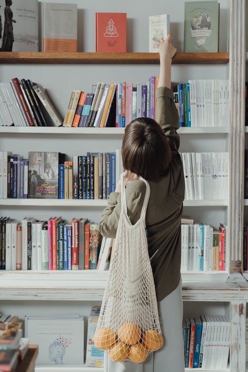 米色的长袖衣服，站在白色的木制书架前的女人 · 免费素材图片