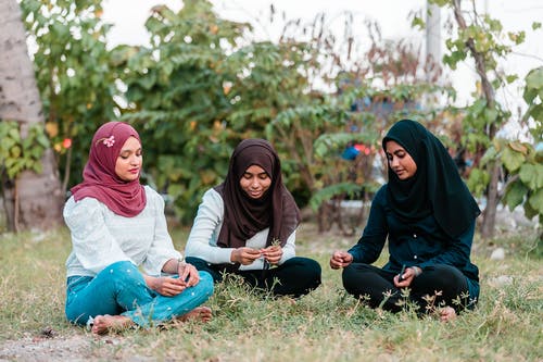高兴的穆斯林妇女谈话和在公园的草坪上休息 · 免费素材图片