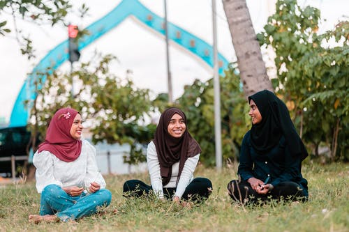 快乐的穆斯林妇女聊天，在公园草地上休息 · 免费素材图片