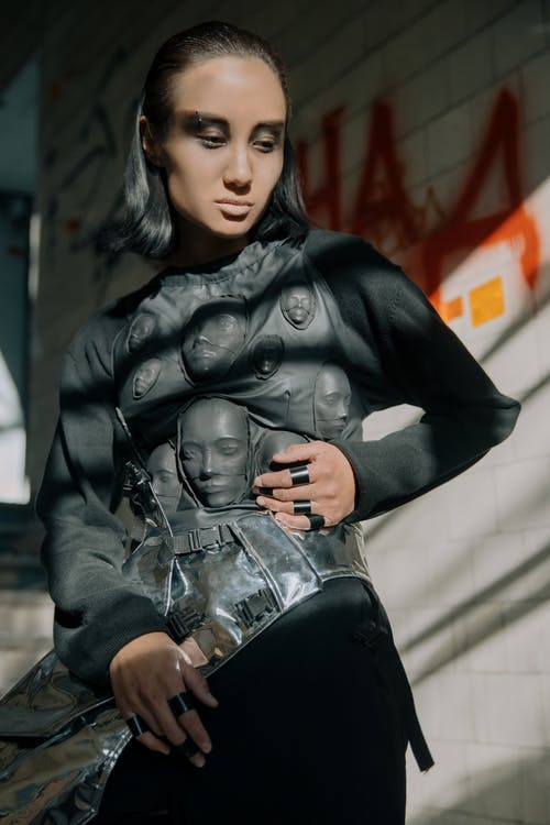 坐在白色的混凝土墙上的黑色皮夹克和黑色牛仔牛仔裤的女人 · 免费素材图片