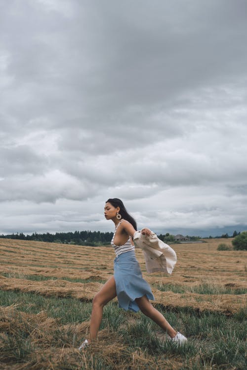 在多云的天空下的草地上运行的族裔女人 · 免费素材图片