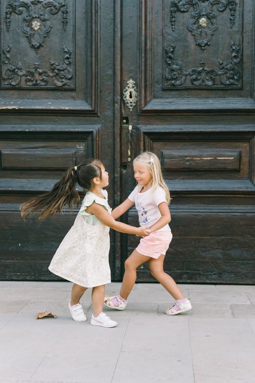 2个女孩站在棕色木门旁边 · 免费素材图片