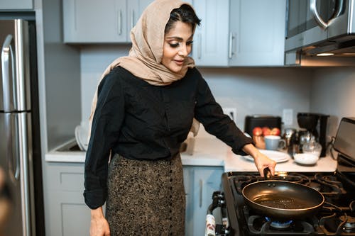 站立与煎锅的美满的阿拉伯妇女在厨房里 · 免费素材图片
