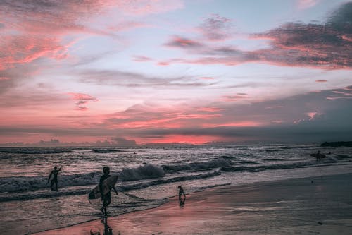 在日落时在沙滩上的冲浪者剪影 · 免费素材图片