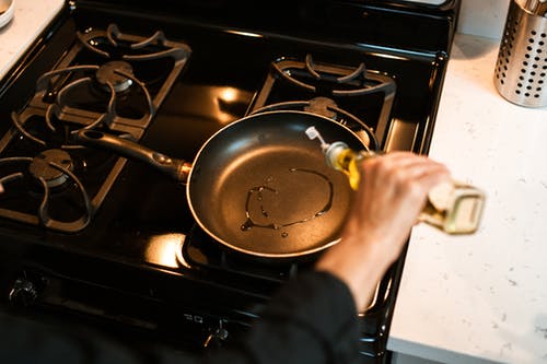 作物无法辨认的厨师在平锅里倒油 · 免费素材图片