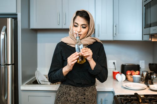 内容阿拉伯女人在厨房里的瓶子里嗅到的油 · 免费素材图片