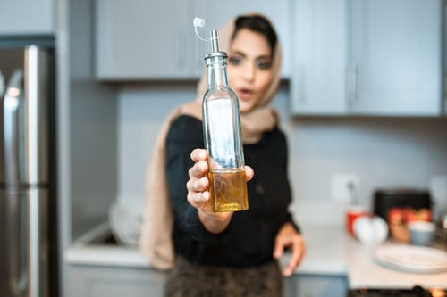 烹饪时展示瓶橄榄油的族裔女人 · 免费素材图片