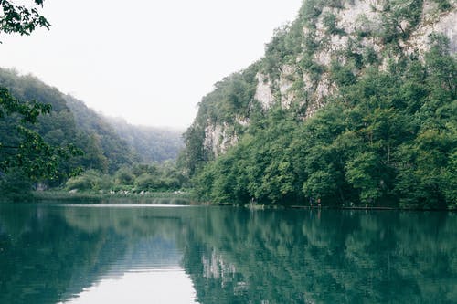 湖面反射绿色山脉在白色的天空下 · 免费素材图片