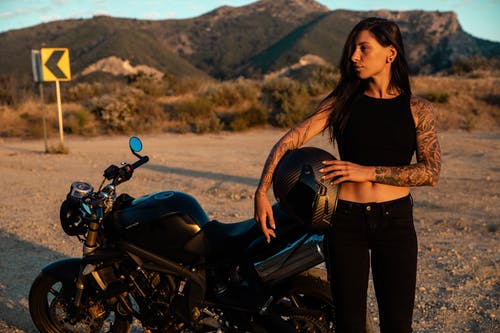 黑色长袖衬衫和黑色牛仔摩托车旁边站着的蓝色牛仔牛仔裤的女人 · 免费素材图片