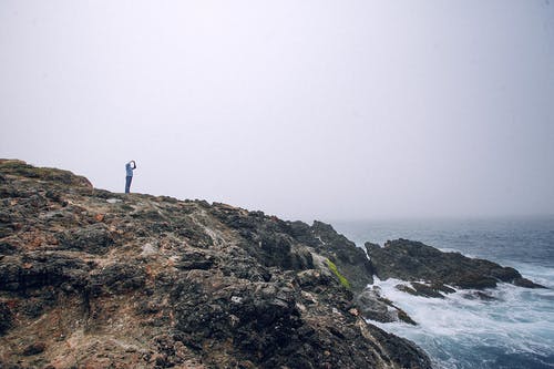 不可识别的旅行者在多岩石的海滨上拍照 · 免费素材图片