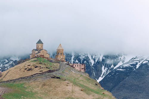 雄伟的山脉包围的草山顶上的中世纪教堂 · 免费素材图片