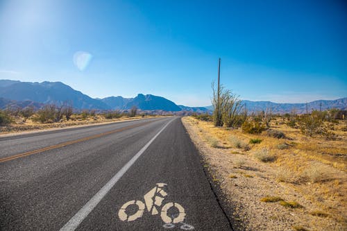 蓝蓝的天空下的绿草田之间的灰色柏油路 · 免费素材图片