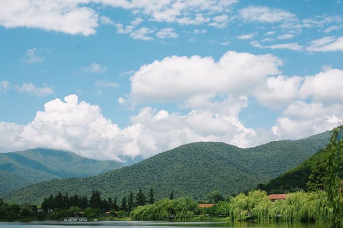 在蓝色多云的天空下湖附近的绿脊 · 免费素材图片