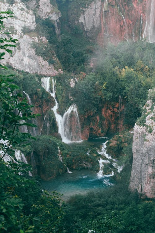 在小池塘附近的绿色山上的快速瀑布 · 免费素材图片
