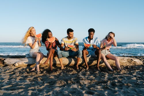 性格开朗的多种族朋友享受在沙滩上的西瓜片 · 免费素材图片