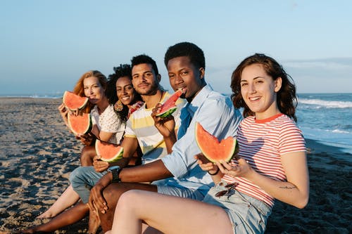很高兴有各种各样的旅行者在海洋海滩上吃西瓜 · 免费素材图片