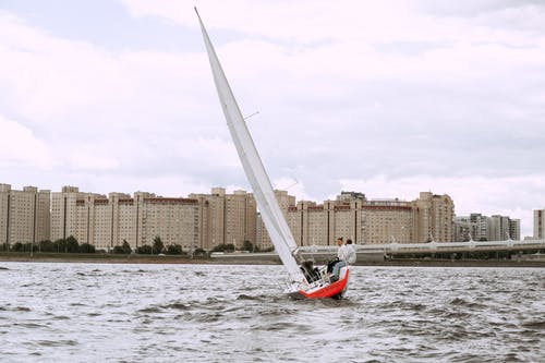 红色和白色的帆船，在城市建筑物附近的水面上 · 免费素材图片