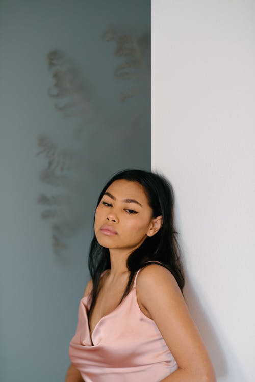 倚在白墙上的沉思亚裔女子 · 免费素材图片