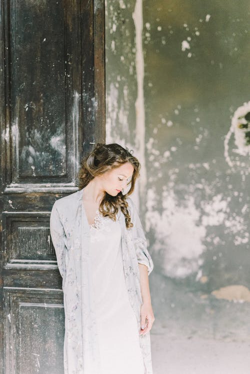 衬衫站在棕色木门旁边的白色按钮的女人 · 免费素材图片