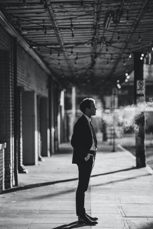 穿着黑色西装的男人站在灰度摄影的人行道上 · 免费素材图片