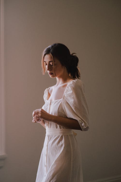 梦幻般的年轻女子，穿着白色连衣裙在明亮的房间里 · 免费素材图片