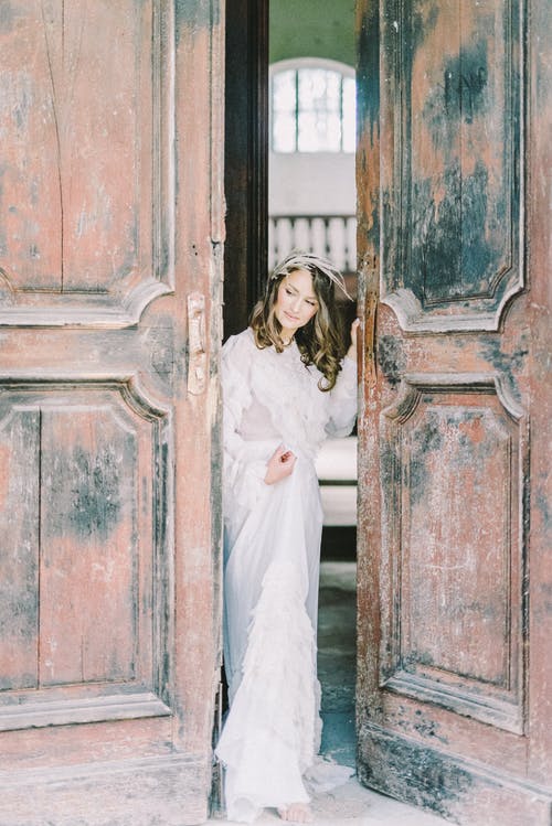 站在棕色木门旁边的白色连衣裙的女人 · 免费素材图片