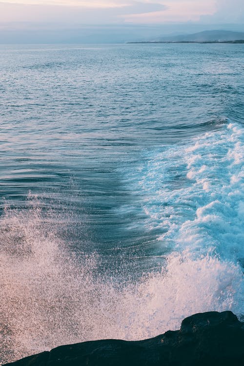 风雨如磐的海浪在日落时分溅在岩石海岸上 · 免费素材图片