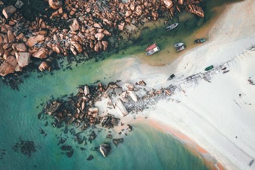 小船在多岩石的海岸附近的水中漂浮 · 免费素材图片