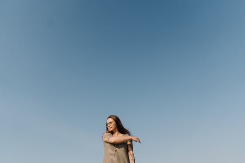 米色无袖连衣裙站在蓝蓝的天空下的女人 · 免费素材图片