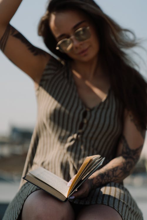 黑色和白色条纹无袖衬衫阅读书中的女人 · 免费素材图片