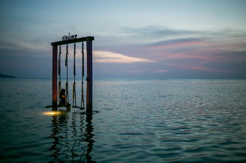 在日落时在海中秋千上的匿名旅行者 · 免费素材图片