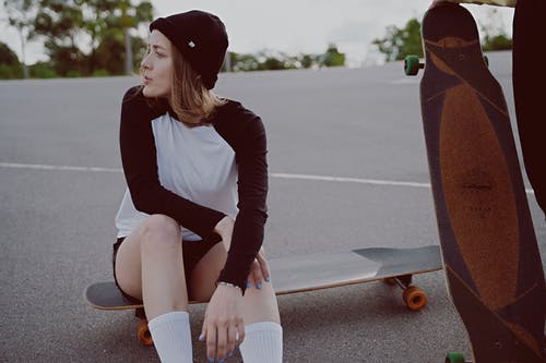 黑色和白色的长袖衬衫和棕色的裤子，坐在棕色滑板期间的女人 · 免费素材图片
