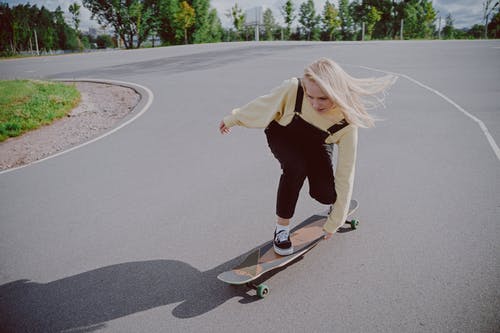 黑色长袖衬衫和黑色的裤子，在灰色的沥青路面上骑滑板的女人 · 免费素材图片