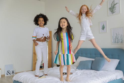 一群可爱有趣的多种族女孩在舒适的床上跳跃 · 免费素材图片