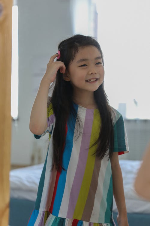 微笑着可爱的亚洲女孩抚摸头发，看着镜子 · 免费素材图片